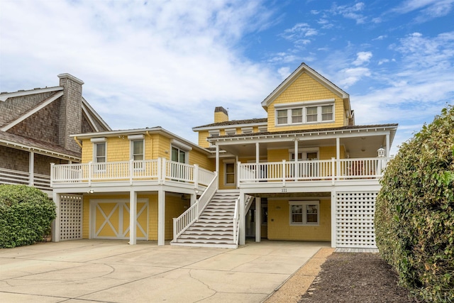 view of front facade featuring concrete driveway, covered porch, stairway, a garage, and a carport