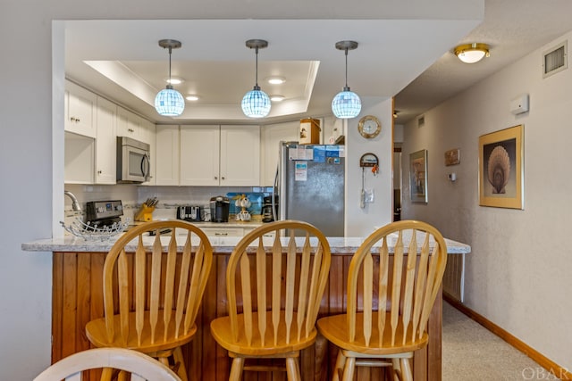 kitchen with stainless steel appliances, a peninsula, visible vents, white cabinetry, and a raised ceiling