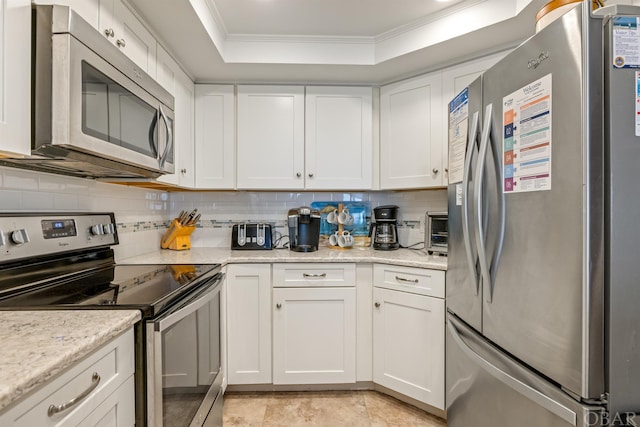 kitchen featuring ornamental molding, appliances with stainless steel finishes, a raised ceiling, and white cabinetry