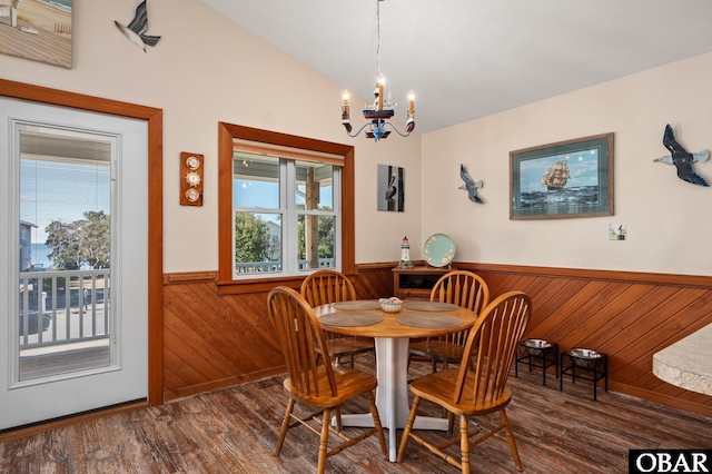 dining room featuring lofted ceiling, a notable chandelier, a wainscoted wall, dark wood-type flooring, and wood walls