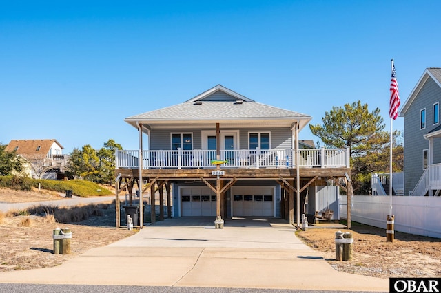 raised beach house featuring a porch, concrete driveway, roof with shingles, and a garage