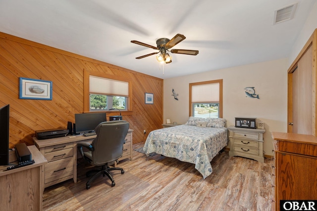 bedroom featuring light wood-type flooring, visible vents, ceiling fan, and wooden walls