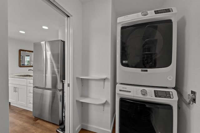 clothes washing area with recessed lighting, laundry area, stacked washer / dryer, wood finished floors, and a sink