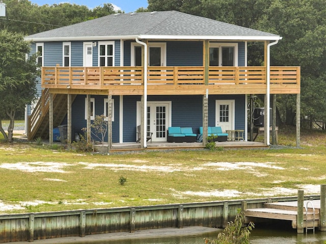 back of property with a shingled roof, a deck with water view, an outdoor living space, a yard, and french doors