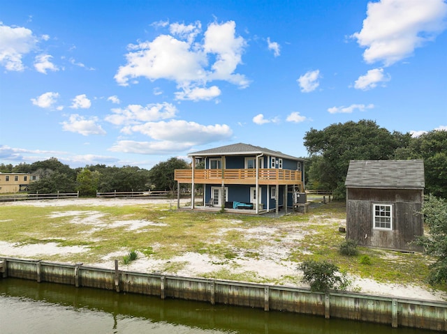 back of property featuring a deck with water view, an outdoor structure, and a shed