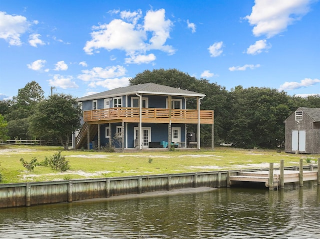 rear view of house with an outbuilding, a deck with water view, stairs, a lawn, and a shed