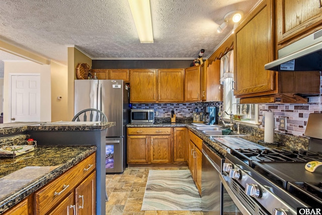 kitchen featuring stainless steel appliances, brown cabinetry, backsplash, and under cabinet range hood