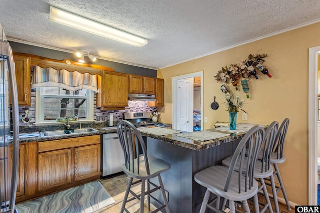 kitchen with brown cabinets, stainless steel appliances, a sink, under cabinet range hood, and a kitchen bar