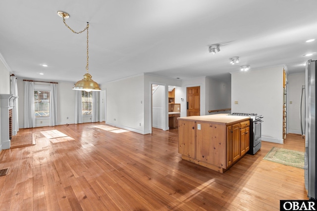 kitchen featuring appliances with stainless steel finishes, a brick fireplace, light countertops, and light wood finished floors