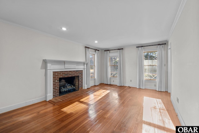 unfurnished living room featuring ornamental molding, a brick fireplace, hardwood / wood-style flooring, and baseboards