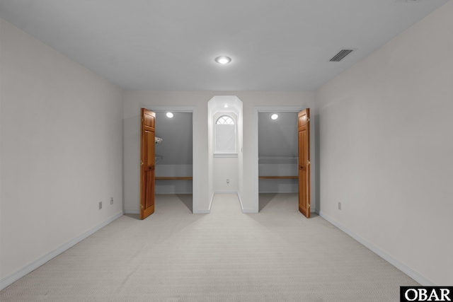 unfurnished bedroom featuring baseboards, a spacious closet, visible vents, and light colored carpet