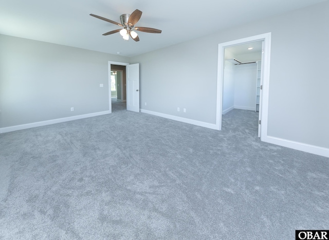 unfurnished bedroom with ceiling fan, a spacious closet, and baseboards