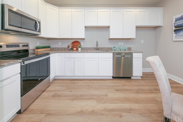 kitchen featuring stainless steel appliances, white cabinetry, a sink, and light stone countertops