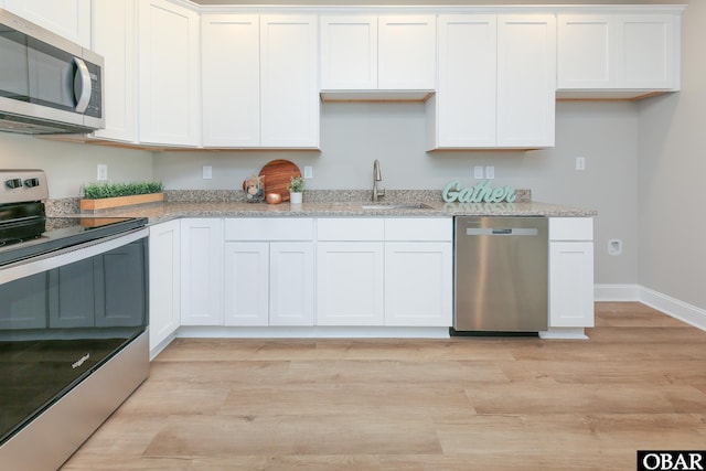 kitchen featuring light stone counters, light wood-style flooring, appliances with stainless steel finishes, white cabinets, and a sink