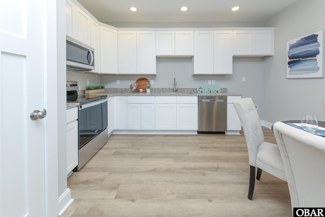 kitchen featuring appliances with stainless steel finishes, white cabinetry, light wood-style floors, and light stone counters