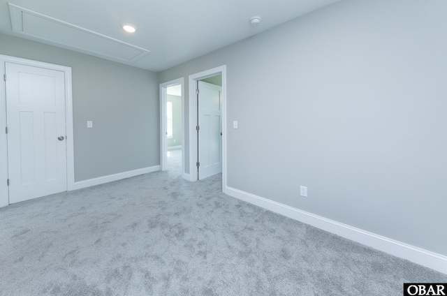 unfurnished bedroom with baseboards, attic access, and light colored carpet