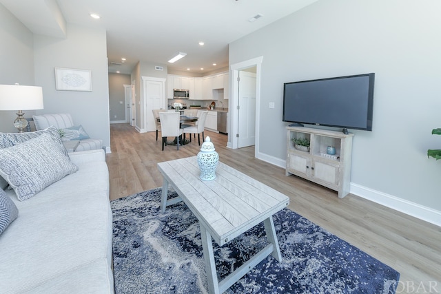 living room with light wood-type flooring, visible vents, baseboards, and recessed lighting