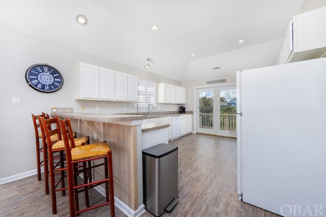 kitchen with white appliances, white cabinets, a kitchen breakfast bar, a peninsula, and light countertops