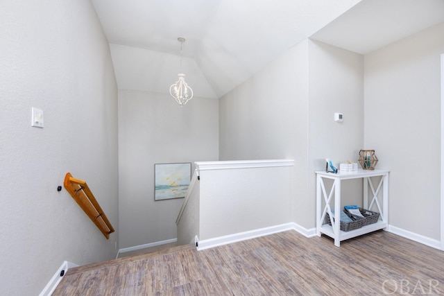 stairs with lofted ceiling, a notable chandelier, wood finished floors, and baseboards