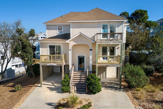 view of front facade with a carport, concrete driveway, roof with shingles, and a balcony