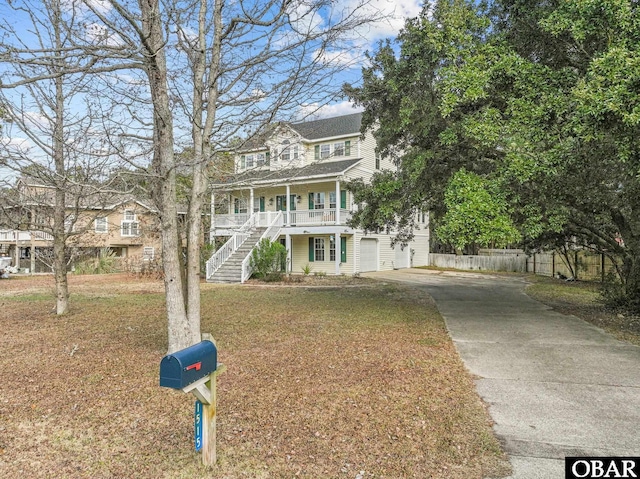 view of front of home with driveway, covered porch, stairs, fence, and a front yard