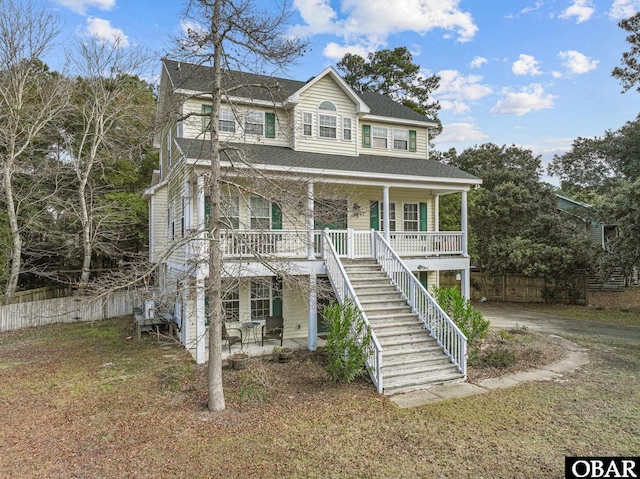 view of front of house with stairway, roof with shingles, covered porch, fence, and a front yard