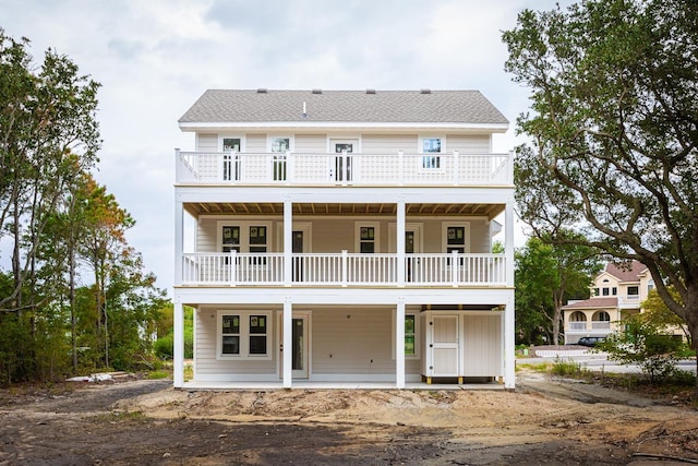 back of property featuring a balcony, a patio area, and roof with shingles