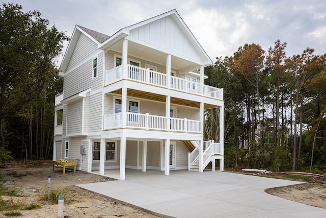 raised beach house with board and batten siding, concrete driveway, a balcony, and a carport