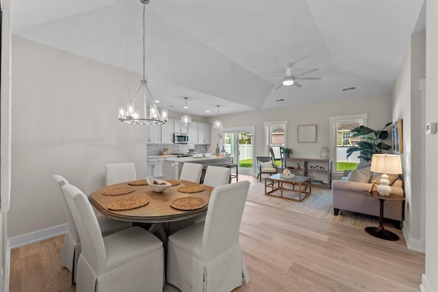 dining room with ceiling fan with notable chandelier, visible vents, baseboards, vaulted ceiling, and light wood finished floors