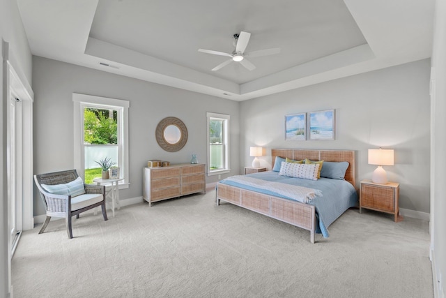 bedroom featuring a raised ceiling, light colored carpet, and multiple windows