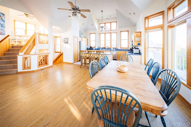 dining space with an inviting chandelier, light wood-style flooring, stairway, and high vaulted ceiling