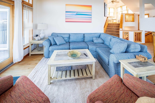 living room featuring light wood finished floors, stairway, a wealth of natural light, and a ceiling fan