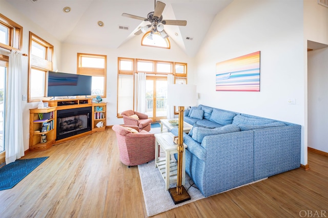 living area featuring ceiling fan, high vaulted ceiling, a fireplace, wood finished floors, and visible vents