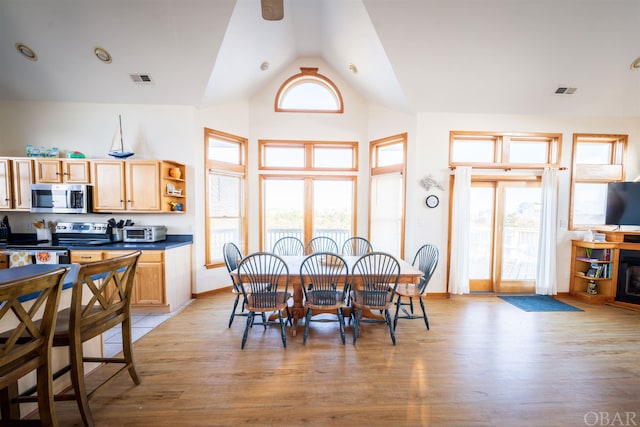 dining room with high vaulted ceiling, a toaster, visible vents, and light wood-style flooring