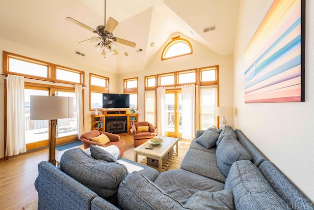 living area featuring light wood-type flooring, high vaulted ceiling, a fireplace, and visible vents