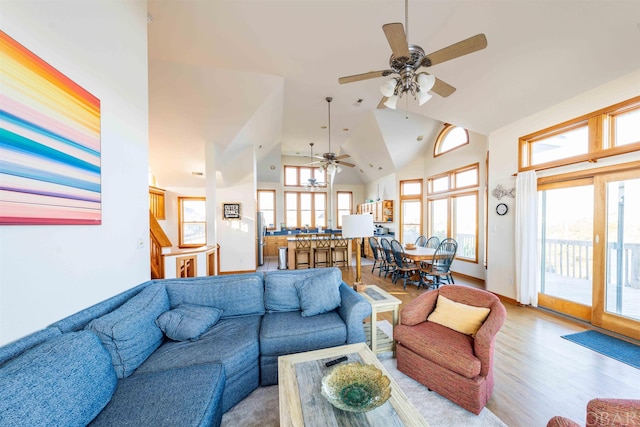 living room with light wood-style floors, ceiling fan, high vaulted ceiling, baseboards, and stairs