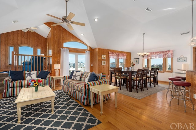 living room featuring ceiling fan with notable chandelier, wood walls, wood finished floors, and visible vents