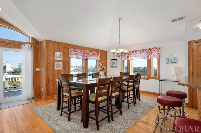 dining space with wood walls, light wood-style flooring, visible vents, and a notable chandelier