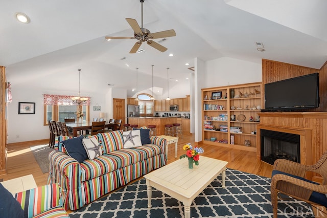 living room with light wood-style floors, a fireplace, high vaulted ceiling, and ceiling fan with notable chandelier