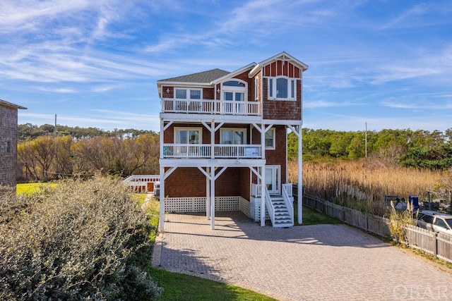 coastal inspired home featuring a balcony, driveway, fence, and stairway