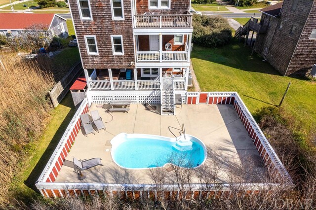 rear view of house with an outdoor pool, a patio, a balcony, a fenced backyard, and a yard