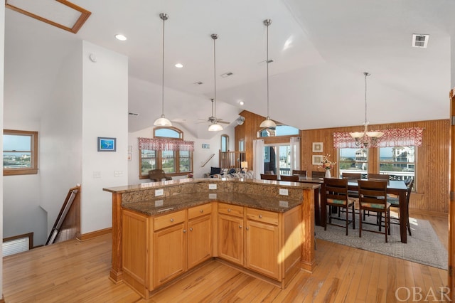 kitchen with pendant lighting, light wood finished floors, dark stone counters, and a center island