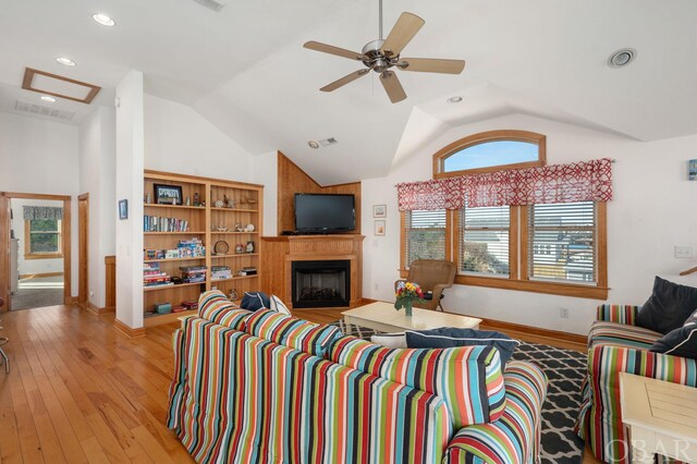 living room featuring lofted ceiling, a large fireplace, a ceiling fan, baseboards, and light wood-style floors