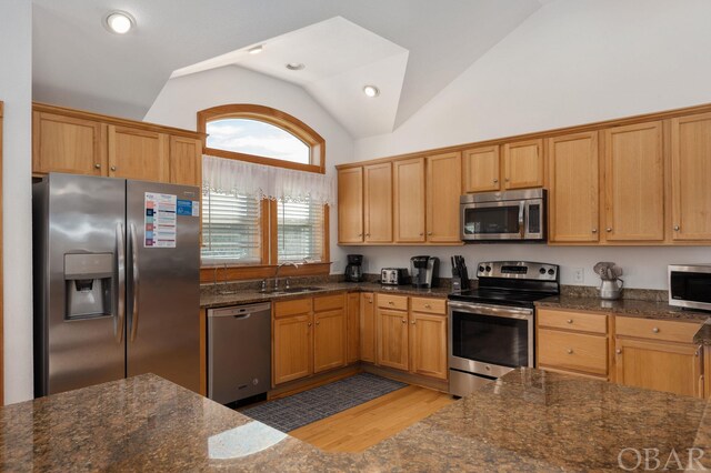 kitchen featuring vaulted ceiling, appliances with stainless steel finishes, dark stone counters, and a sink