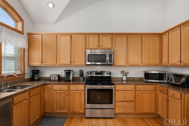 kitchen featuring lofted ceiling, dark stone countertops, stainless steel appliances, light wood-type flooring, and a sink