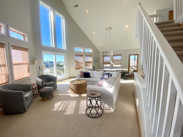 living area featuring visible vents, light carpet, plenty of natural light, and stairway