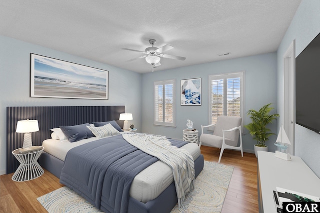 bedroom featuring visible vents, a textured ceiling, a ceiling fan, and wood finished floors