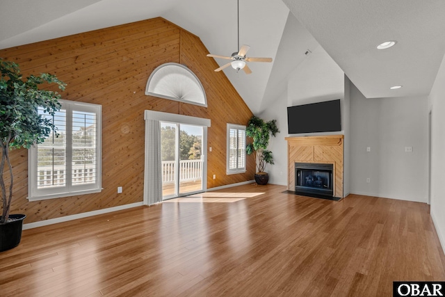 unfurnished living room with wooden walls, a fireplace, high vaulted ceiling, and wood finished floors