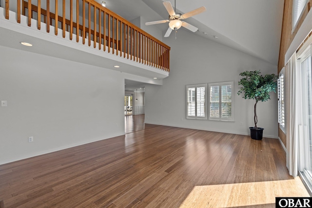 unfurnished living room with ceiling fan, baseboards, wood finished floors, and a towering ceiling