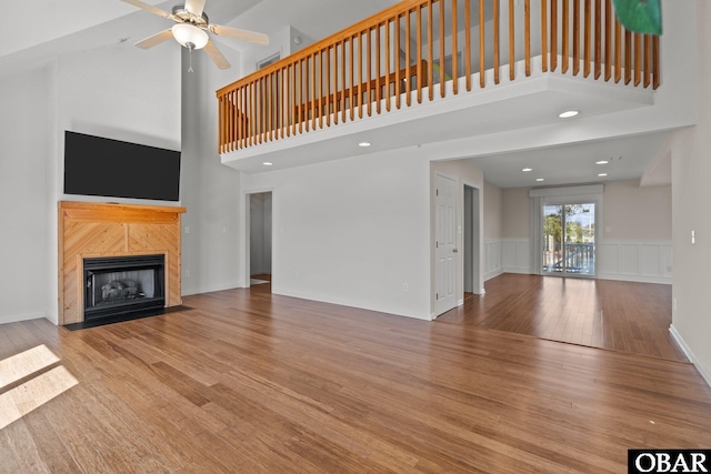 unfurnished living room featuring a fireplace, a high ceiling, ceiling fan, and wood finished floors